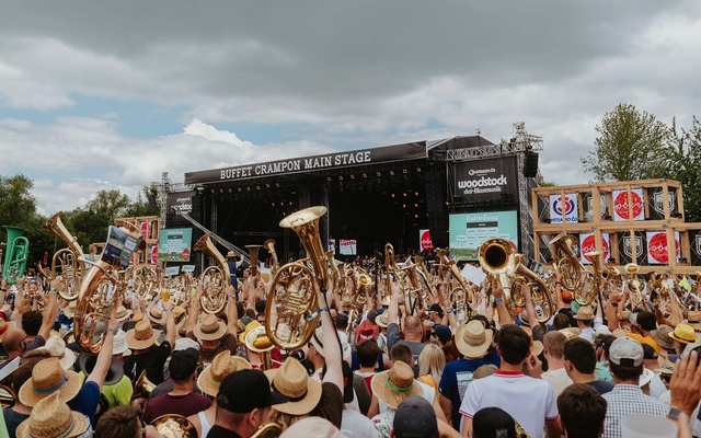 Menschenmenge mit Blasinstrumenten vor einer Open-Air-Bühne beim Woodstock der Blasmusik.