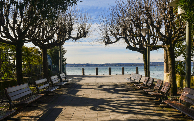 Winterliche Promenade in Sirmione am Gardasee mit kahlen Bäumen und Bänken entlang des Weges.