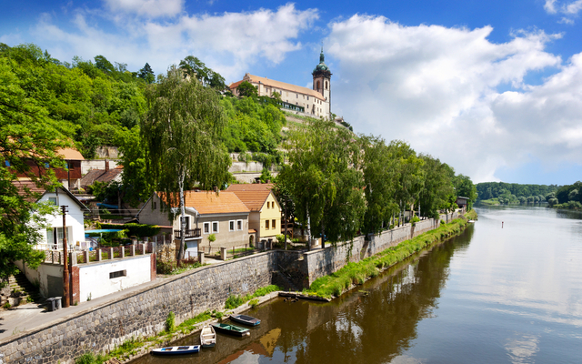 Fluss mit Häusern am Hang, Kirche im Hintergrund, blauer Himmel.