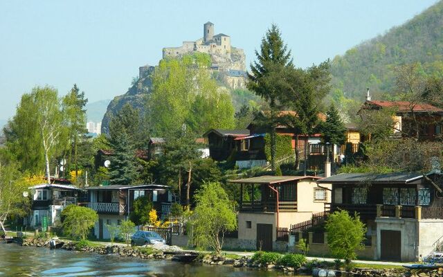 Blick auf die Burg Strekov auf einem Hügel über der Elbe, umgeben von Bäumen und Häusern.
