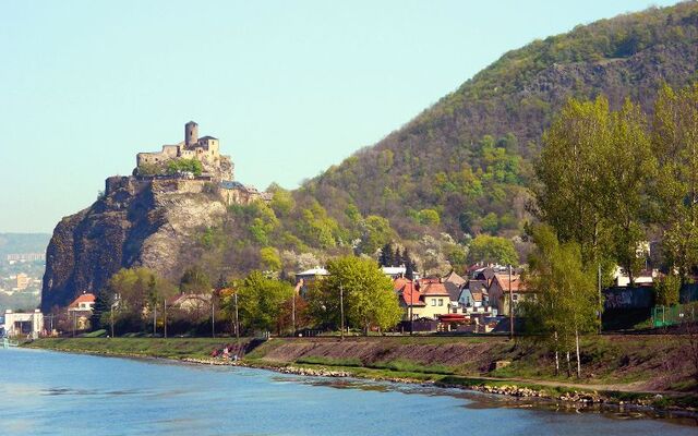 Burg Strekov auf einem Hügel über der Elbe, umgeben von Bäumen und Wohnhäusern.