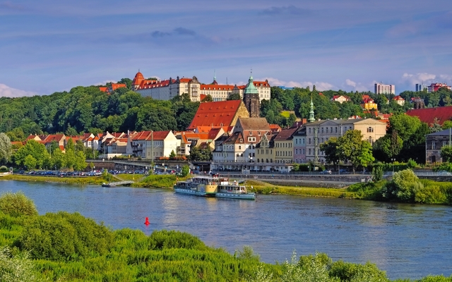 Historische Stadtansicht mit Fluss und Schloss im Hintergrund.