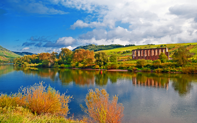 Flusslandschaft mit bewölktem Himmel und Ruinen im Hintergrund.