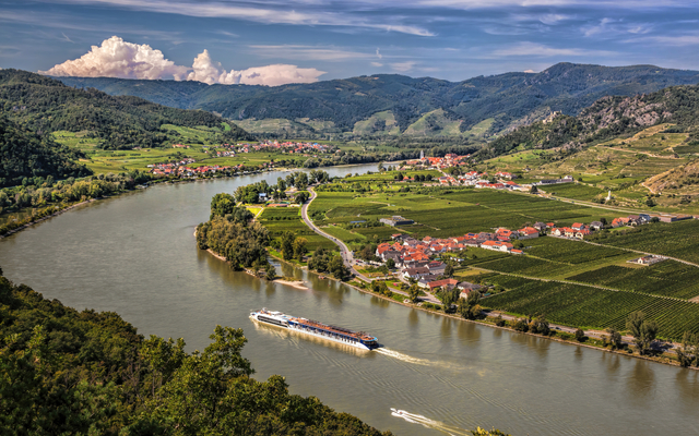 Flusslandschaft mit Schiff in hügeliger Gegend und Weinbergen.