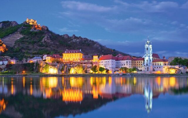 Abendliche Stadtansicht mit Kirche und Hügeln am Flussufer, Spiegelung im Wasser.