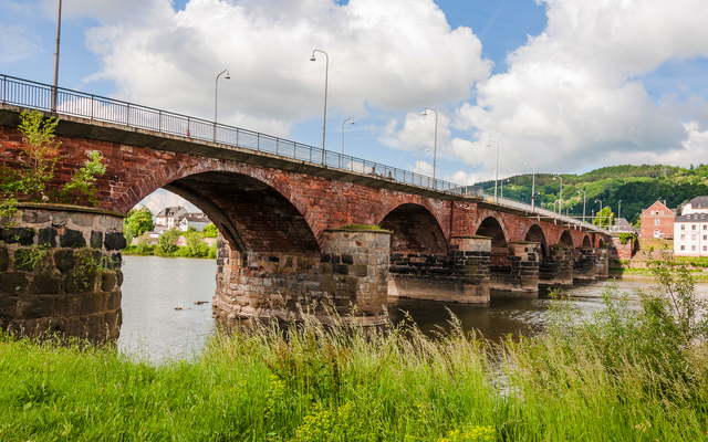 Steinbrücke über einen Fluss mit bewölktem Himmel im Hintergrund.