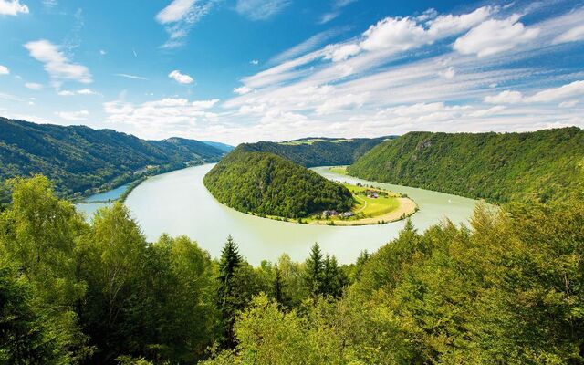 Fluss mit Biegung, umgeben von bewaldeten Hügeln und blauem Himmel.