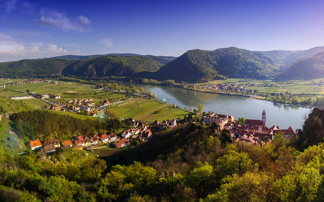 Panorama einer grünen Flusslandschaft mit Hügeln und Dörfern.